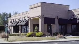 Exterior view of a single-story brick commercial building with black awnings and landscaping.